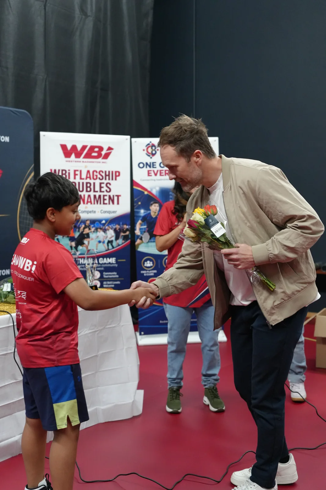 A young Team WBi member welcoming Clint with flowers and a handshake