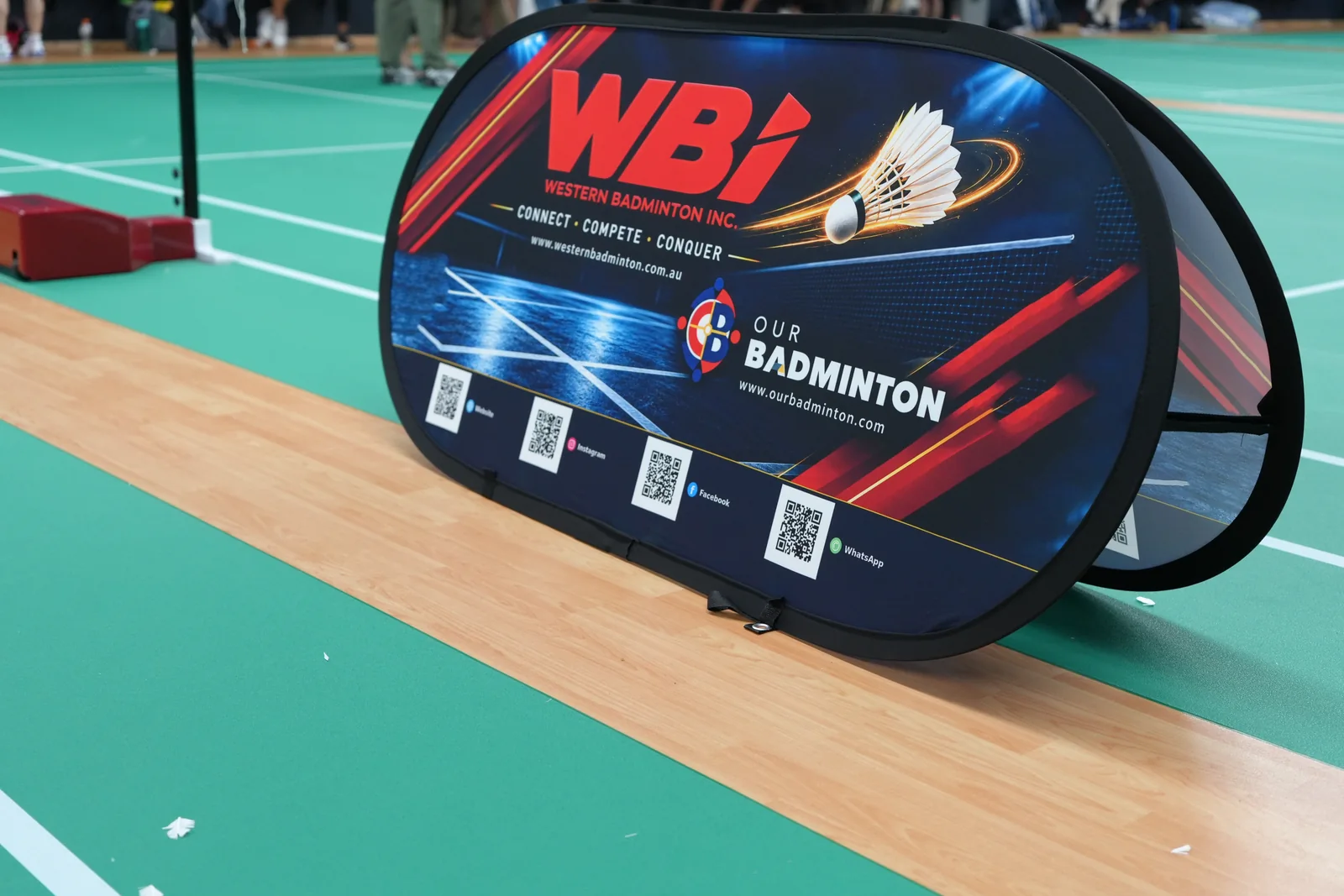 WBi and Our Badminton branding beside the badminton court
